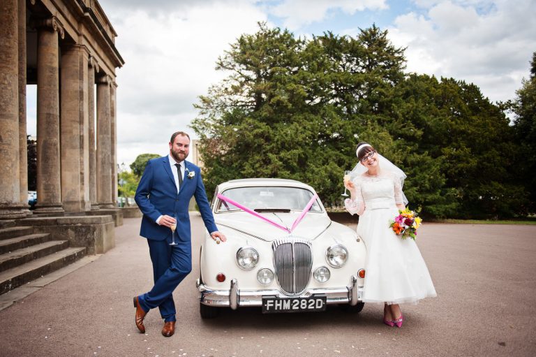 Bride and groom stand with their amazing classic car outside the front of the Pittville Pump Rooms.