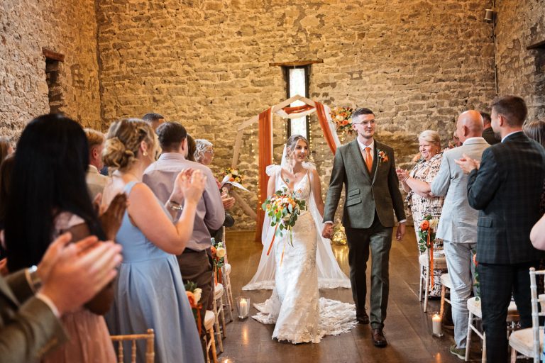 Bride and groom exit the wedding ceremony being congratulated by friends and family at Priston Mill.