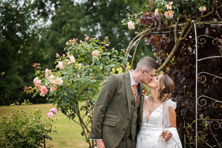 Bride and groom kiss by the rose arch at Priston Mill, Bath.