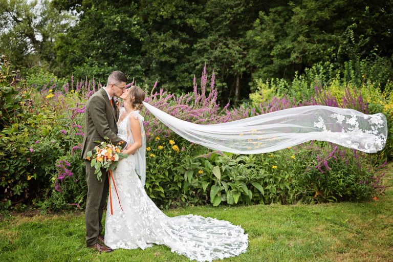 Bride and groom kiss with wedding veil in the air.