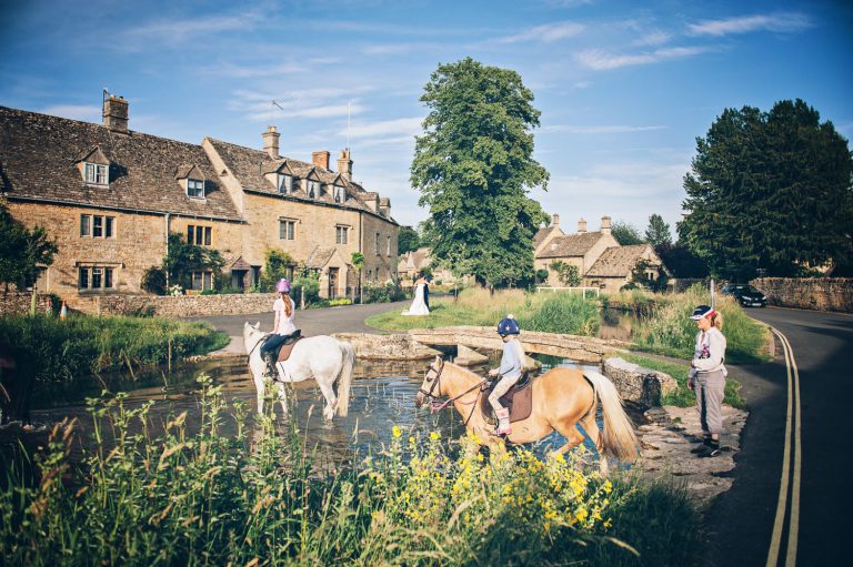 Idyllic Cotswold wedding scene with horses crossing the stream at The Slaughters Country Inn