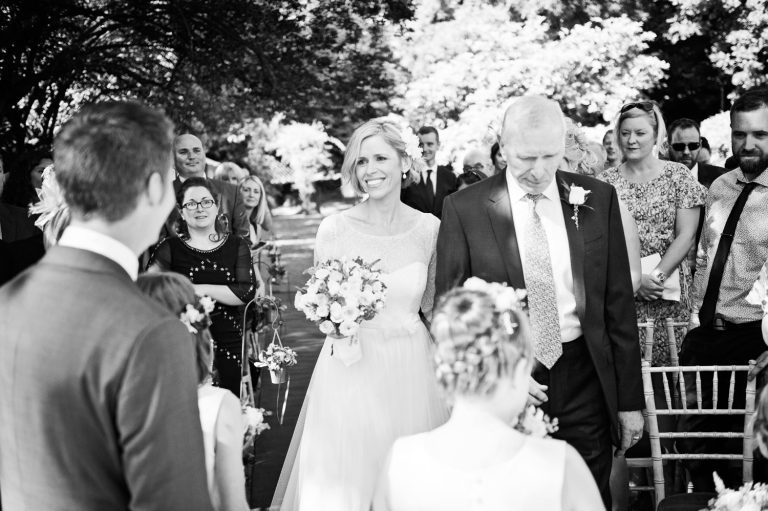 B&W photo of the bride walking down the wedding isle as she approaches her husband to be.