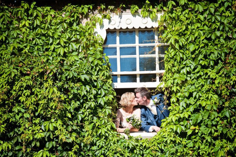 Bride and groom kiss as they hang out of a window.
