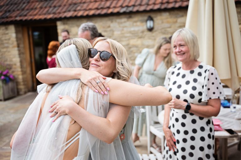 Candid photo Bride getting hugged by friend at Kingscote Barn.