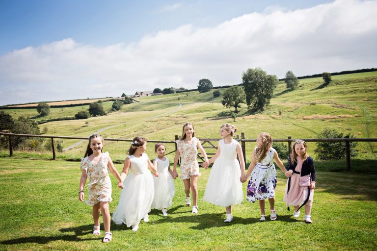 Lots of kids holding hands and walking in the green fields.