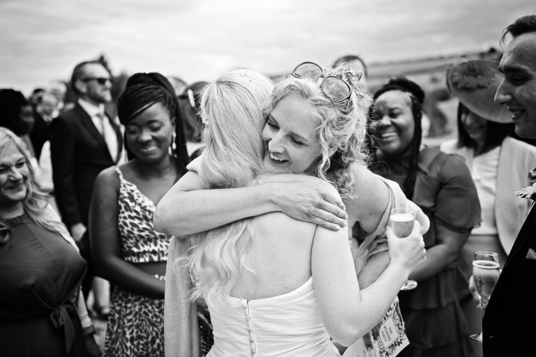 Candid moment at a wedding at Kingscote Barn - friend hugging the bride. B&W image.