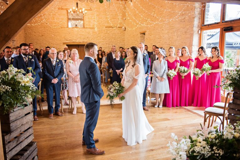Bride and groom saying their wedding vows to each other with their friends and family behind them at Kingscote Barn.
