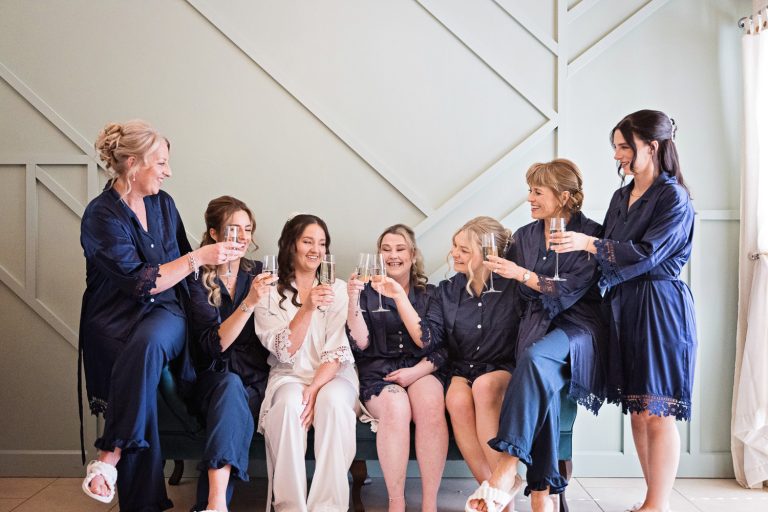 Bride and bridesmaids and mums laughing together in the bridal suite at Kingscote Barn.