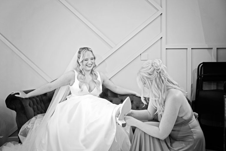 Bride getting her shoes on by her bridesmaid.