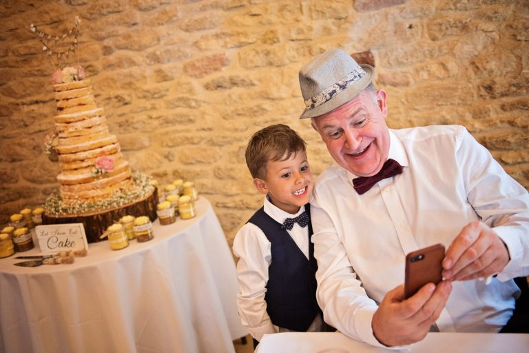 Fun candid photo of wedding guests doing a selfie with the wedding cake behind them.