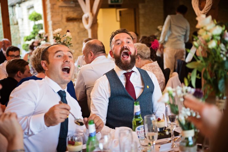 Candid fun photo during wedding breakfast at Kingscote Barn of guests throwing raspberry at each other.