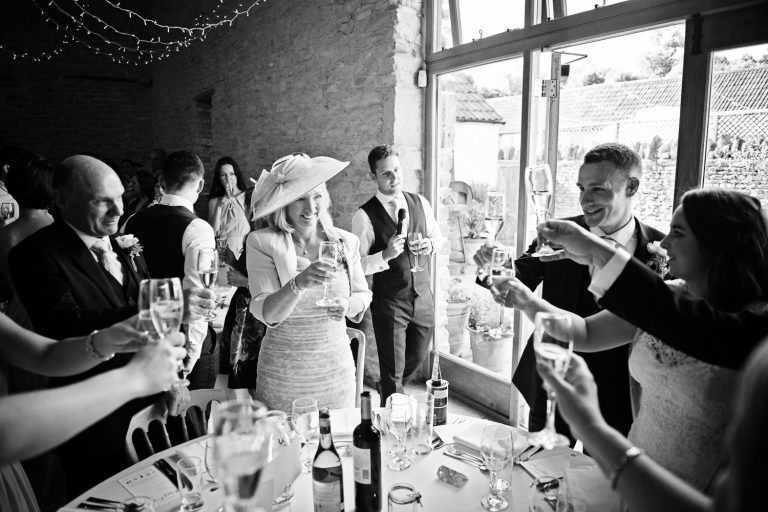Story telling image of wedding guests raising a glass at the end of speeches at Kingscote Barn.