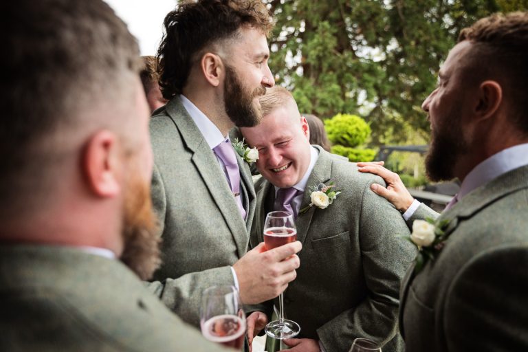 Storytelling candid image of wedding groom being comforted whilst he is being emotional at Tewkesbury Park