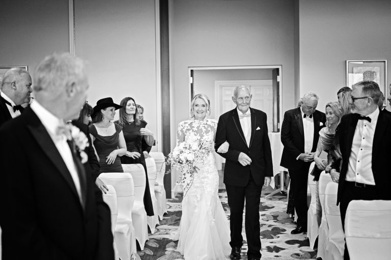 B&W image of bride walking down the wedding isle at Tewkesbury Park with her father.