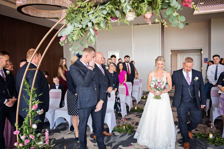 Bride walks down the wedding isle at Tewkesbury Park hotel. Groom is crying.