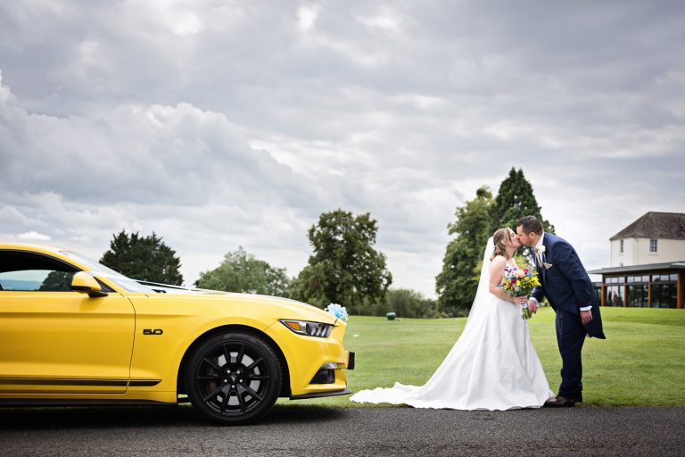 Bride and groom next to a smart yellow car in front of the Cotswold Suite at Tewkesbury Park.