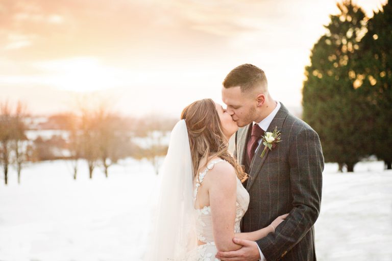 Bride and groom grab a moment in the grounds at Tewkesbury Park. Winter scene with snow in the background.