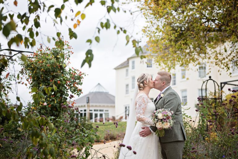 Bride and groom kiss in the gorgeous gardens at Tewkesbury Park in Autumn.