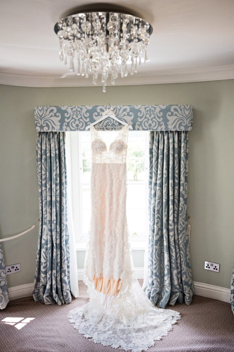 Portrait photo of a brides wedding dress hung up in the window in King Richard 111 room at Tewkesbury Park.