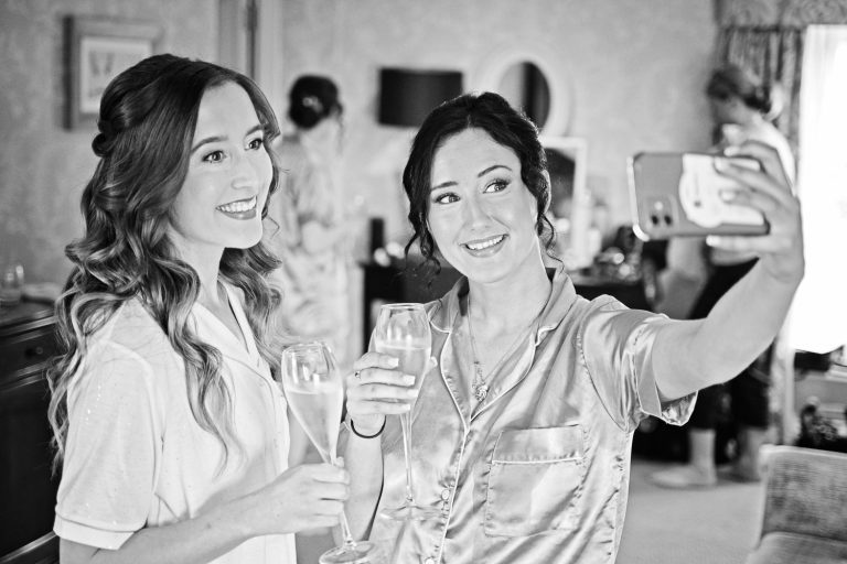 Candid B&W photo of bride and bridesmaid doing a selfie.