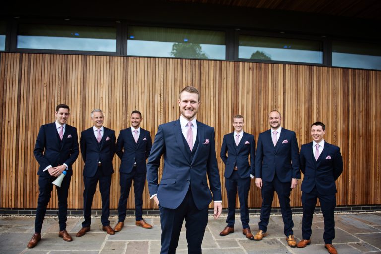 Groom and groomsmen pose in front of a wooden cedar wall for a wedding at Tewkesbury Park Hotel.