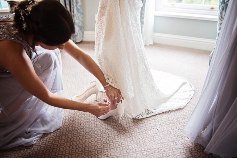 Close up documentary photo of bride having her wedding shoes put on by her bridesmaid.