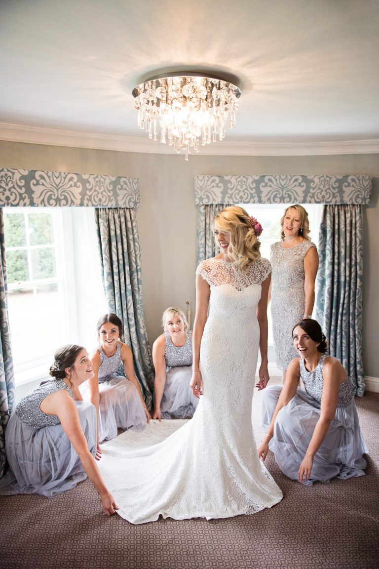 Candid photo of bridesmaids looking after the bride in her wedding dress at Tewkesbury Park.