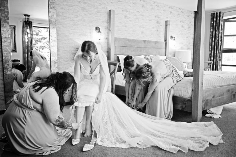 Bride puts on her wedding shoes with the help of the bridesmaids. B&W photo.