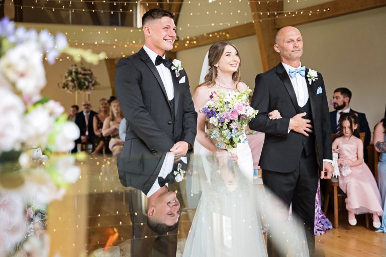 Bride and groom and father of the bride stand in front of their wedding guests during their wedding ceremony at The Mill Barns.