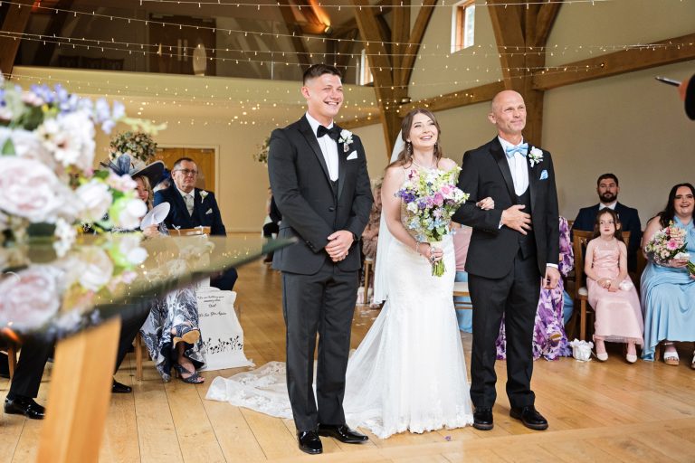 Bride and groom and father of the bride stand in front of their wedding guests during their wedding ceremony at The Mill Barns.