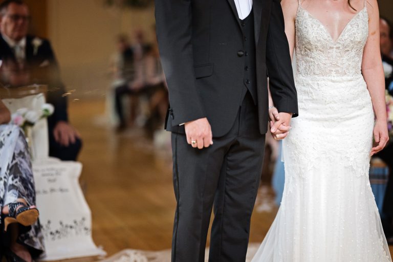 Bride and groom hold hands close up.
