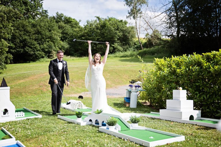 Bride raising her hands in the air winning against her groom at crazy golf.