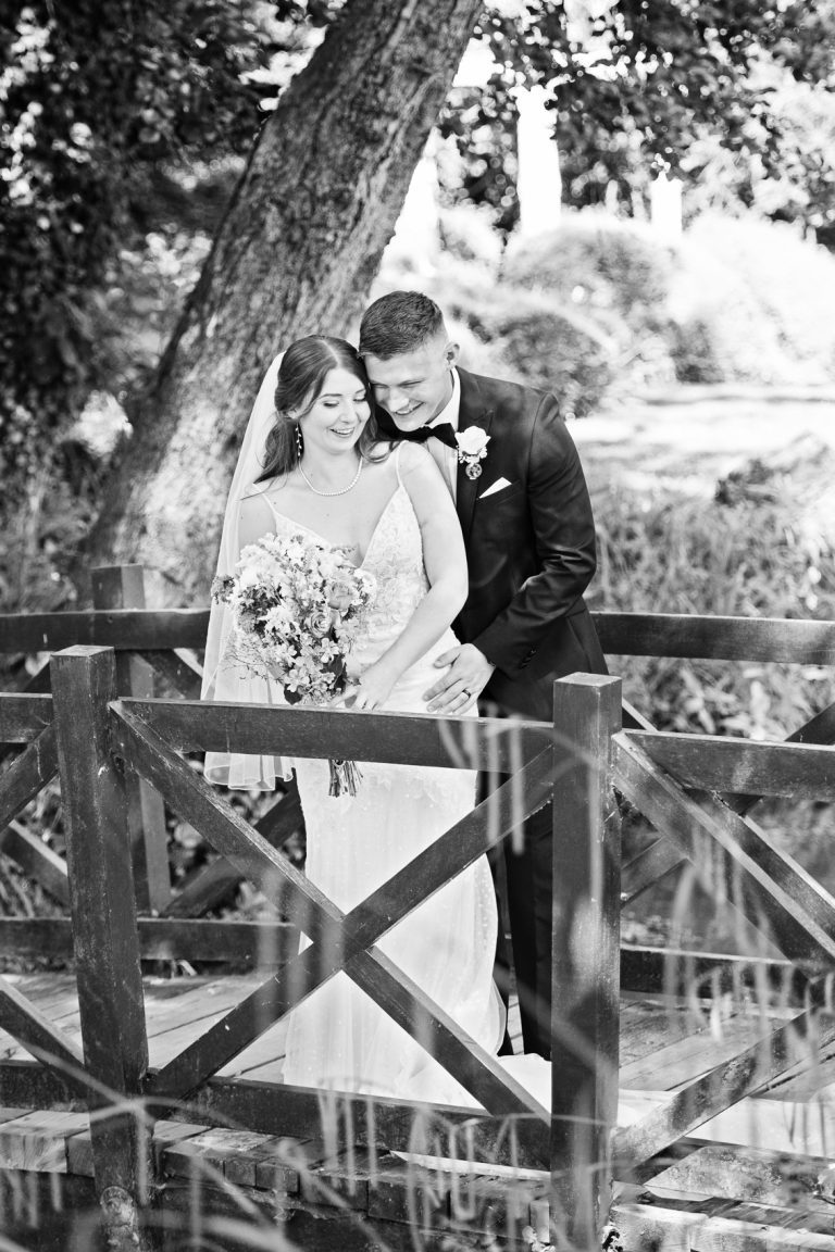Classic portrait photo of bride and groom standing on a wooden bridge at The Mill Barns.