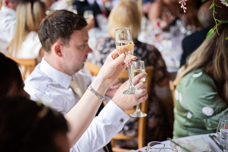 Weddings guests raise their champagne glasses in celebration to at the wedding.