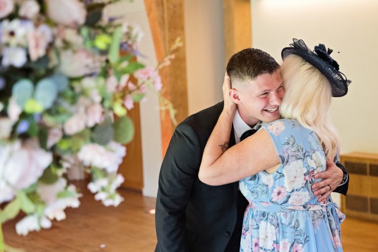 Wedding guest hugging the groom. Floral flowers to the left of the image.