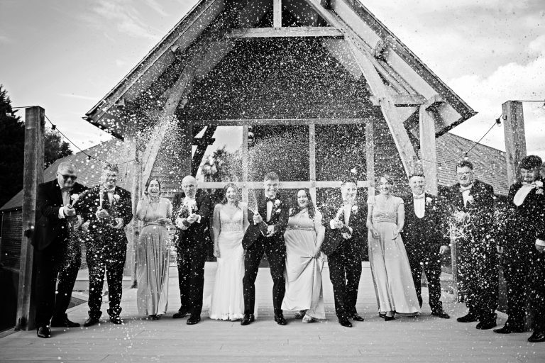 B&W photo of the bridal party spraying champagne at the photographer outside the front of The Mill Barns.