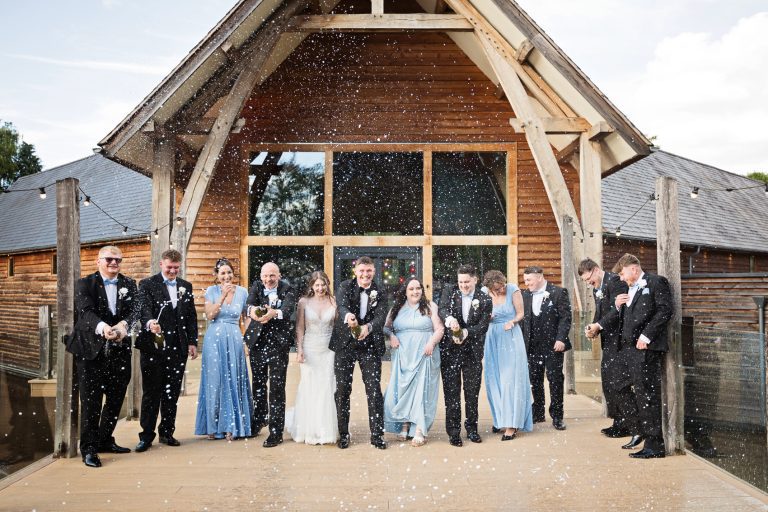 Bridal party spray champagne at the wedding photographer outside The Mill Barns.